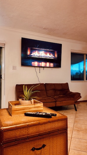 A living room with a flat-screen TV mounted on the wall, a brown sofa, a wooden chest of drawers, and a potted plant. - Canal-Front Keys Retreat with Jacuzzi • Sleeps 12 (Big Pine Key)