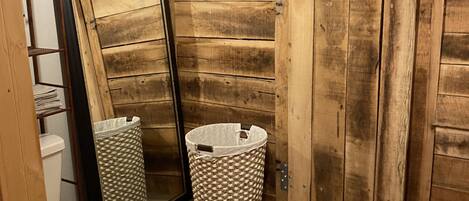 Un baño con suelo de madera, inodoro blanco, armario de madera y un espejo apoyado en la pared.
