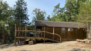 A wooden cabin with a wooden deck and a metal gate, surrounded by trees. - Deadwood acres cabin #3 (Eminence)