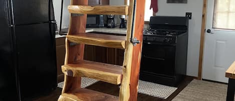 Een houten ladder in een keuken met een koelkast, fornuis en keukenkastjes.