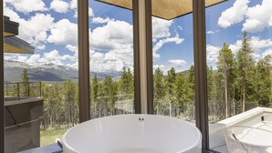 Ein modernes Badezimmer mit einer großen Badewanne, großen Fenstern und Blick auf Berge und Bäume.