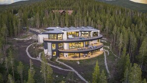 Ein modernes, mehrgeschossiges Haus mit gebogener Form, eingebettet in eine bewaldete Berglandschaft.