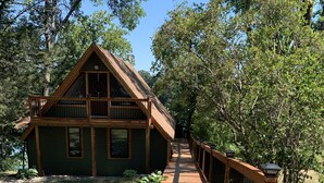 A wooden deck leading to a cabin with a balcony, surrounded by greenery. - Spring thaw-summer is on the horizon!  (Annandale)