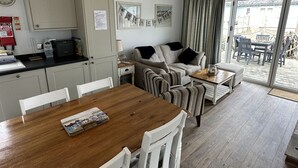 A compact living space with a kitchenette, a sofa set, a dining table, and a sliding glass door leading to an outdoor area. - Stunning Beach House - Sleeping 4 in 2 Bedrooms - Pool and Beach Access Included. (Primrose Valley)