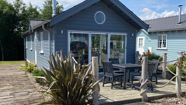 A blue house with a deck, a circular window, and a chimney. - Stunning Beach House - Sleeping 4 in 2 Bedrooms - Pool and Beach Access Included. (Primrose Valley)