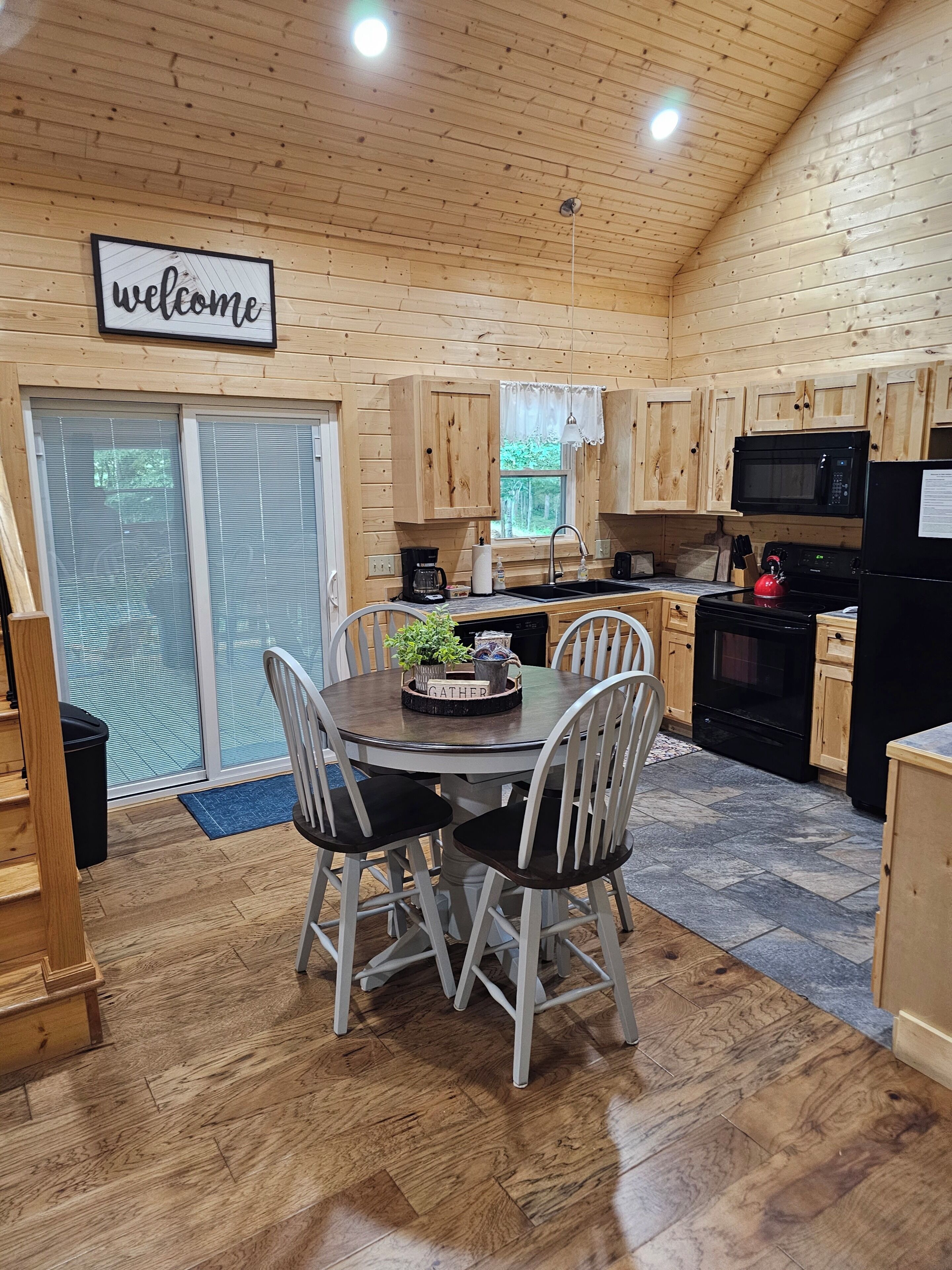 Un intérieur en bois comprenant une table à manger, des chaises, un coin cuisine équipé d’appareils électroménagers et un panneau d’accueil.