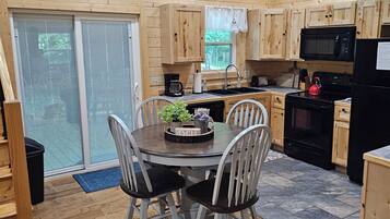 A wooden interior with a dining table, chairs, a kitchen area with appliances, and a welcome sign.
