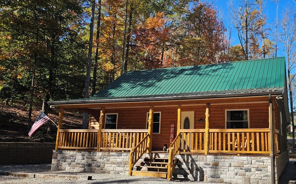 Une cabane en bois avec un toit vert, des fondations en pierre et une véranda en bois dotée d’une balustrade.