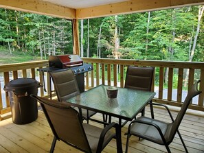 Une terrasse extérieure couverte, équipée d’une table et de chaises, d’un barbecue et d’une poubelle.