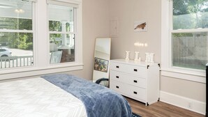 A bedroom with a bed, dresser, and large windows.