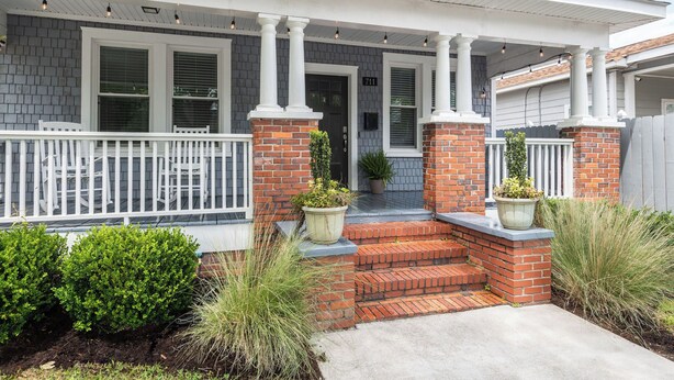 A residential house with a porch, brick columns, and potted plants.