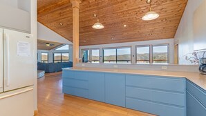 A modern kitchen with a large island, wooden ceiling, and large windows offering a view of the hills.