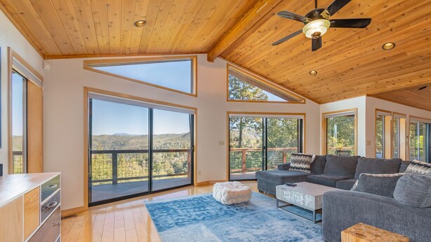 A spacious living room with a large sliding glass door leading to a balcony, a ceiling fan, and a wooden floor.
