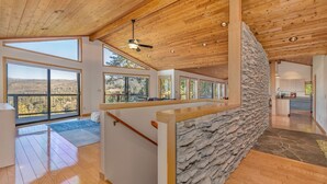 A spacious living area with a stone accent wall, large windows, and a wooden ceiling.
