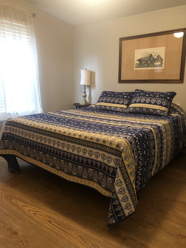 A bedroom with a large bed, a bedside table with a lamp, and a framed picture on the wall.