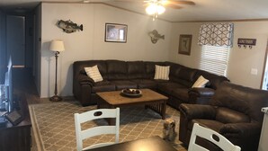 A living room with a brown leather sectional sofa, a wooden coffee table, and two white chairs. - Slice of Heaven 3/2 camp on lakefront w/ boathouse (Zwolle)