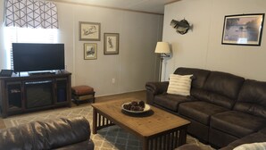 A living room with a flat-screen TV, leather sofas, a coffee table, and framed artwork on the walls. - Slice of Heaven 3/2 camp on lakefront w/ boathouse (Zwolle)