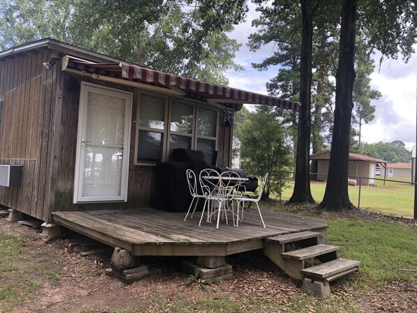 A rustic cabin with a porch, a grill, and a covered outdoor seating area.