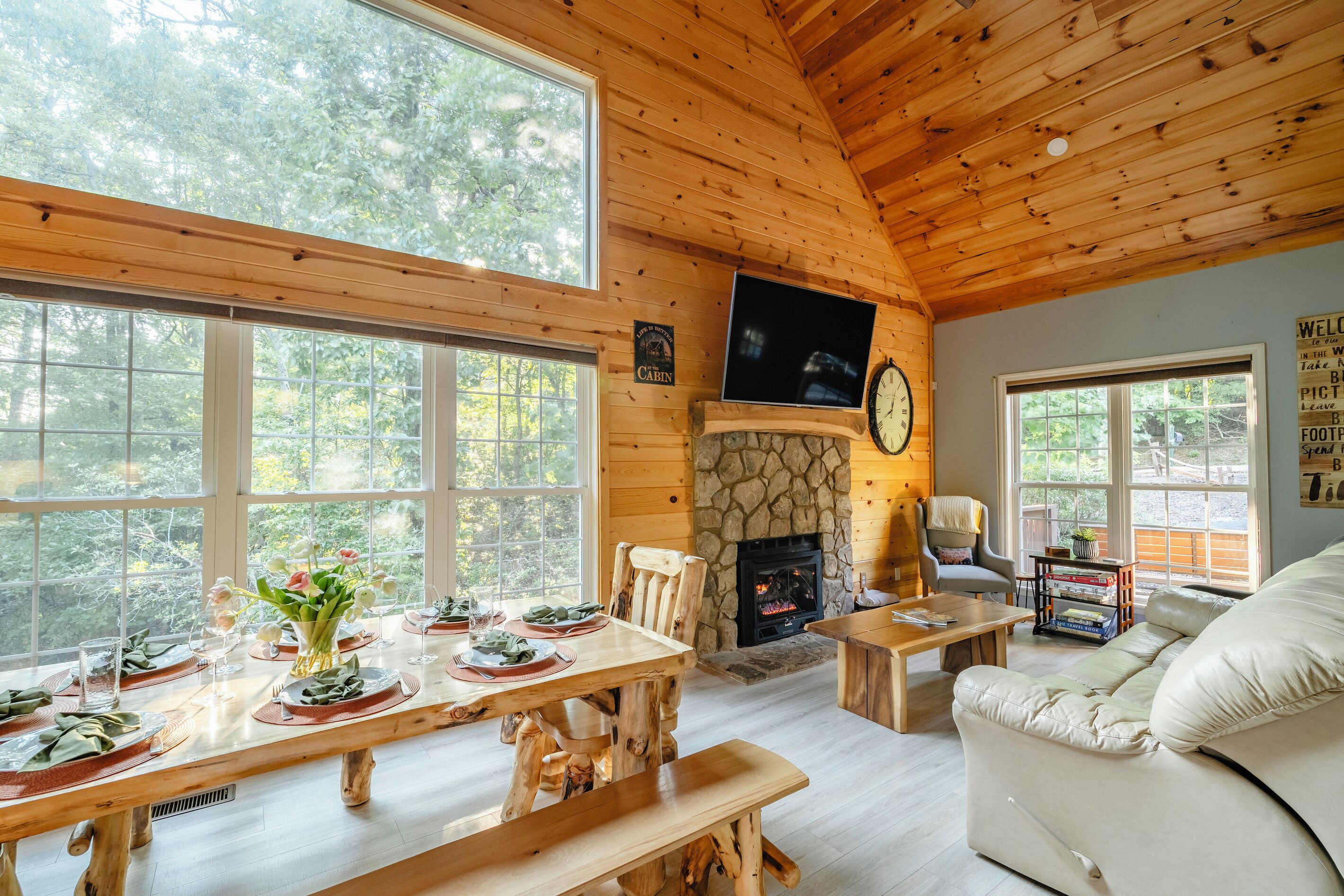 A cabin interior with a stone fireplace, wooden dining table, and a sofa.