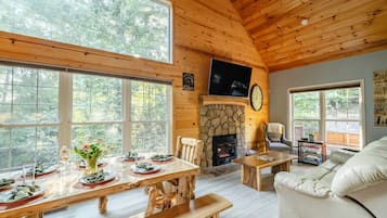 A cabin interior with a stone fireplace, wooden dining table, and a sofa.