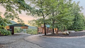 A rustic cabin with a covered porch, surrounded by trees and a gravel driveway.