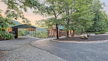 A rustic cabin with a covered porch, surrounded by trees and a gravel driveway.
