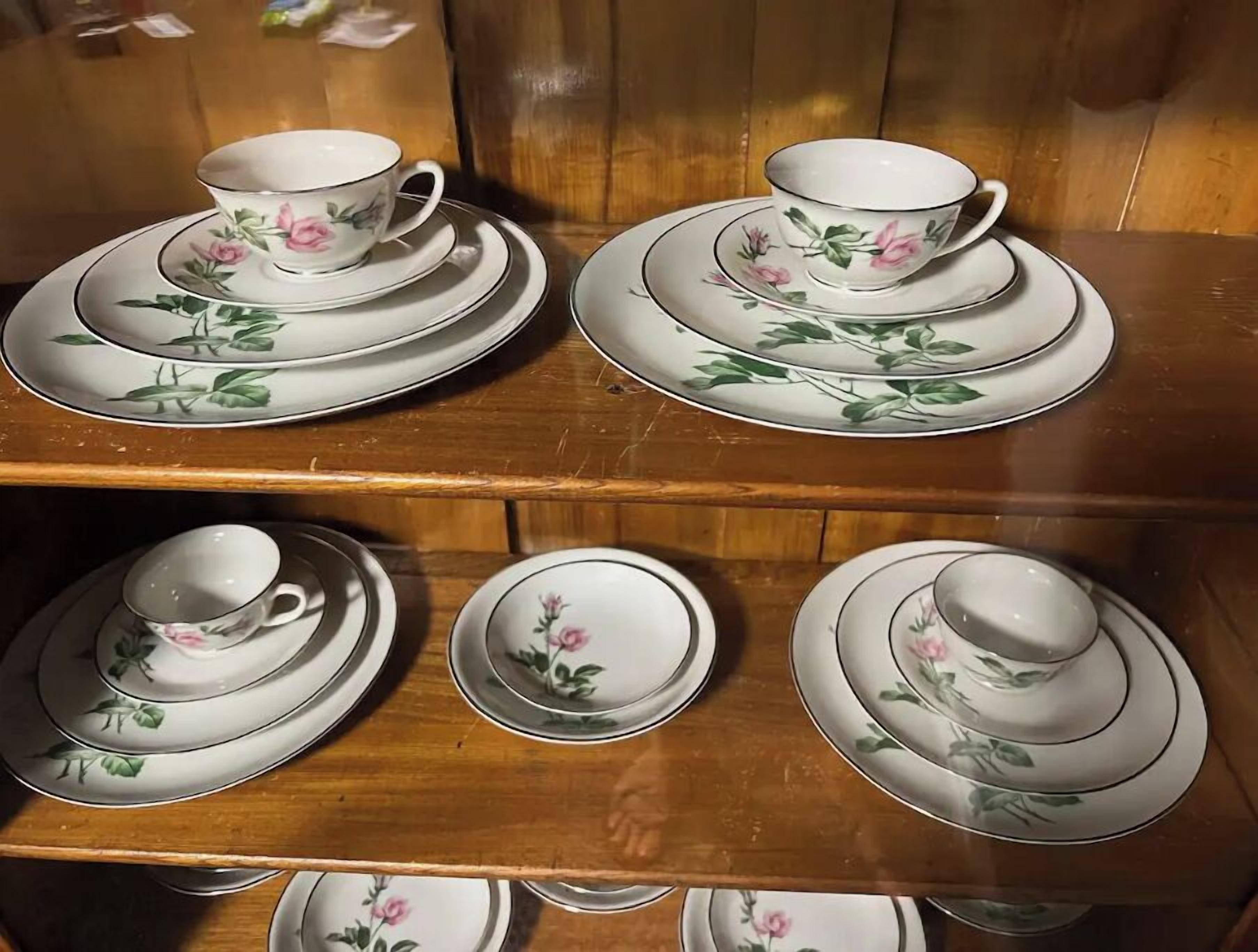 A wooden shelf with multiple sets of white porcelain tea cups and saucers, each adorned with floral designs.