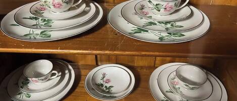 A wooden shelf with multiple sets of white porcelain tea cups and saucers, each adorned with floral designs.