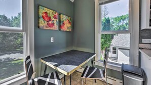 Ein Eckzimmer mit Esstisch und Stühlen, zwei Bildern an der Wand und Blick auf Bäume und ein Haus durch das Fenster.