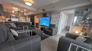 Una sala de estar moderna con un sofá modular, un televisor de pantalla plana y una cocina al fondo.