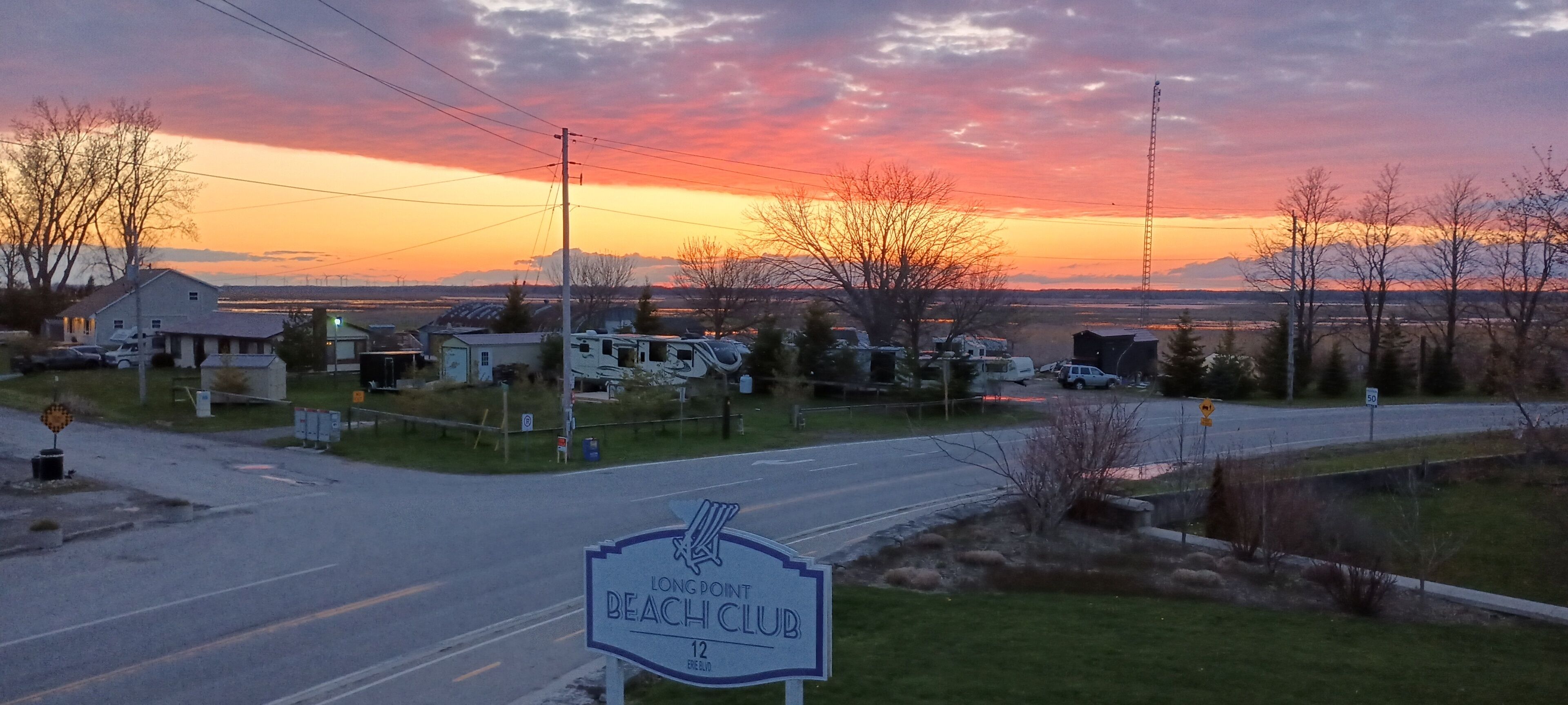 Señal del Long Point Beach Club con vista a una puesta de sol sobre una zona residencial.