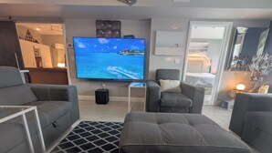 Una sala de estar moderna con un televisor de pantalla plana, sofás grises, un tapete estampado y una mesita.