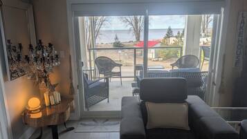 A room with a black leather sofa, a chandelier, and a view of the beach and ocean through a glass door.
