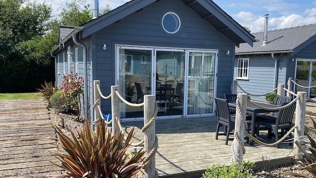 A house with a deck, a dining area with chairs and a table, and a large sliding glass door. - Stunning Beach House - Sleeping 4 in 2 Bedrooms - Pool and Beach Access Included. (Filey)