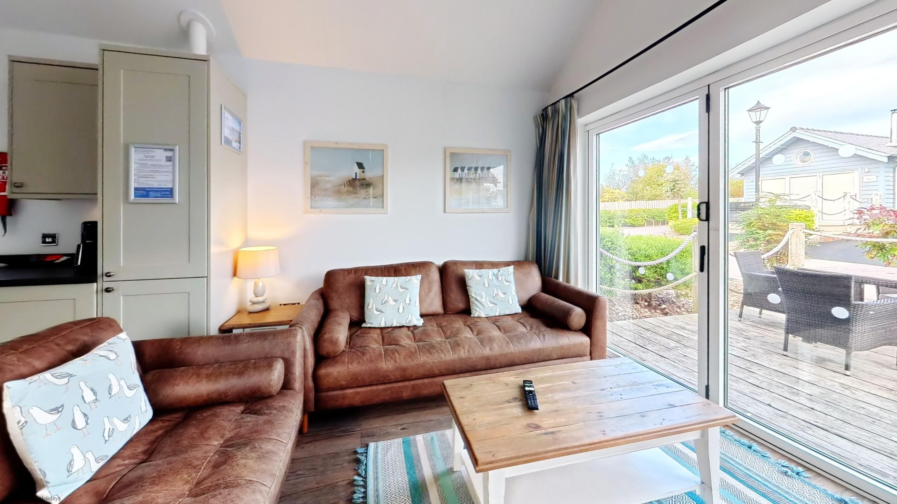 A room with a brown leather sofa, a wooden coffee table, and a view of a house through a large window.
