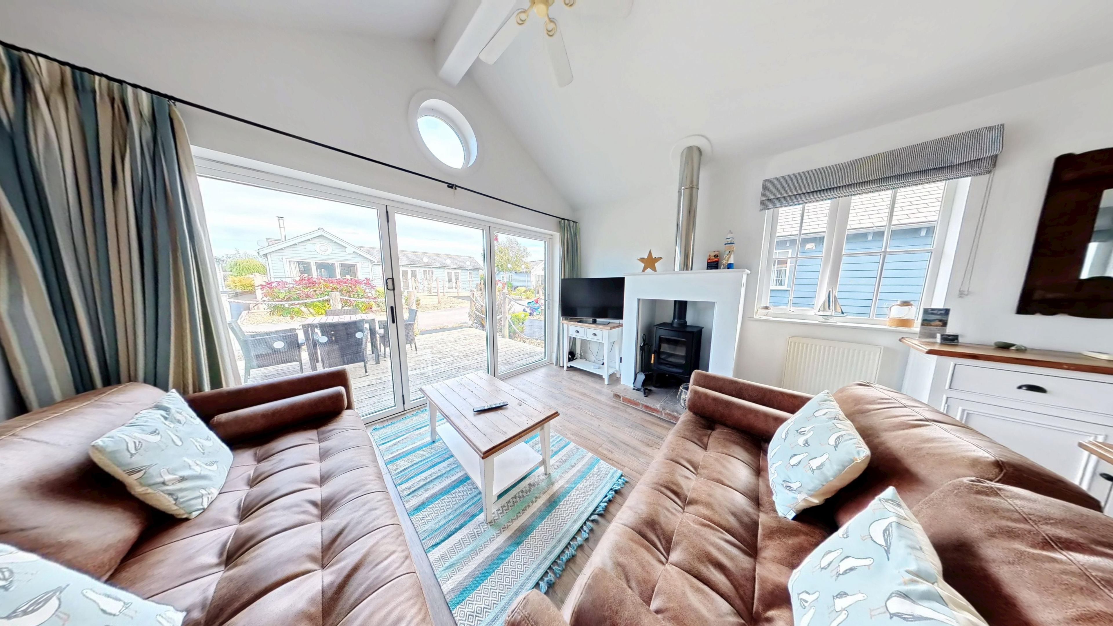 A living room with a sofa set, a television, a fireplace, and a view through the glass doors.