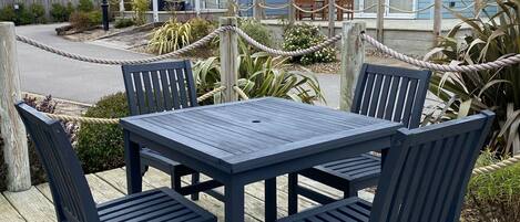 A wooden deck with a table and chairs, a rope barrier, and a house in the background.