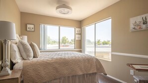 Un dormitorio con una cama grande, dos ventanas, un ventilador de techo y una mesita de noche.