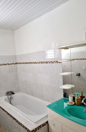 Une salle de bain moderne avec une baignoire, un lavabo en verre et une zone de douche carrelée.