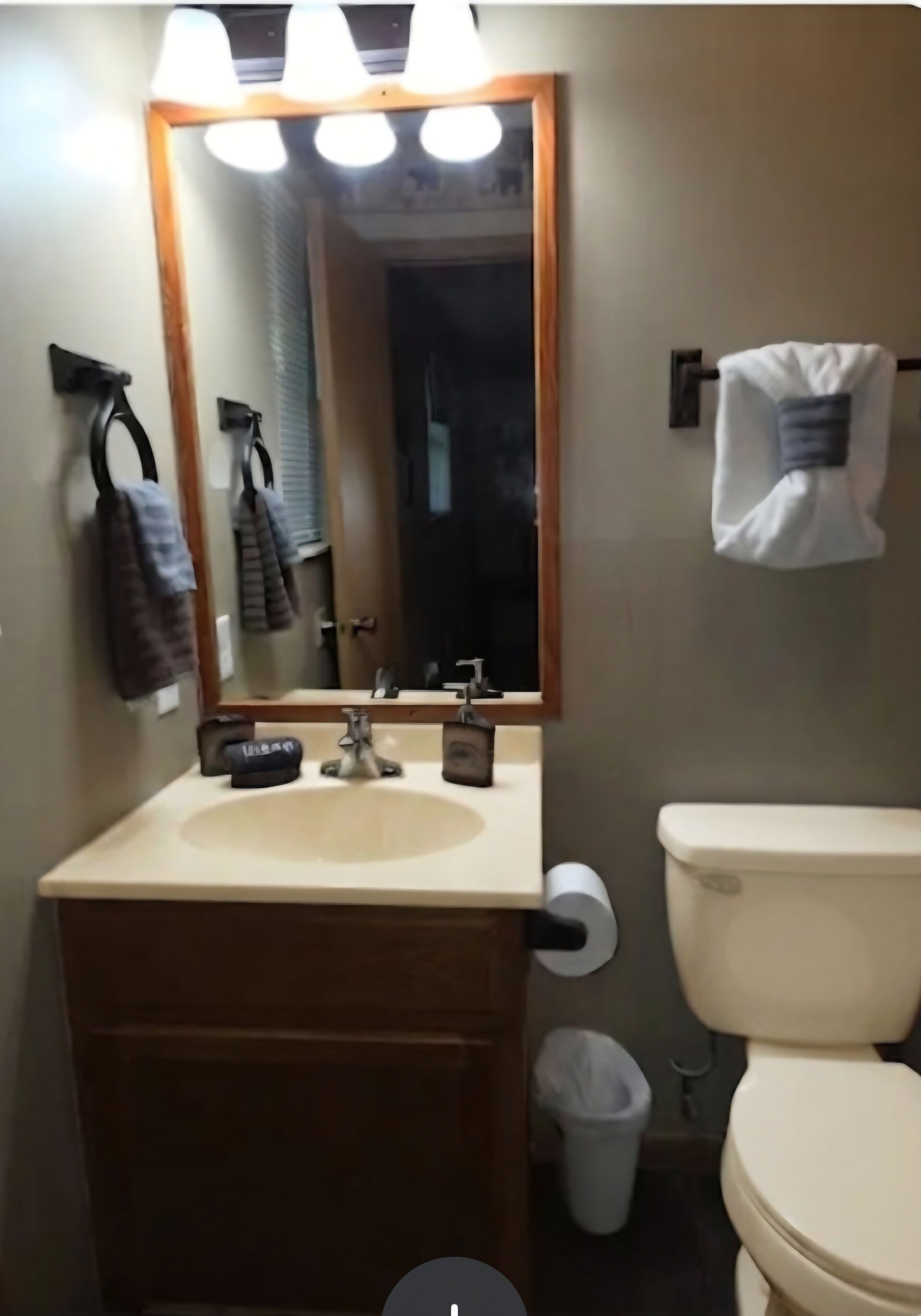 A bathroom with a sink, mirror, toilet, and a trash bin.