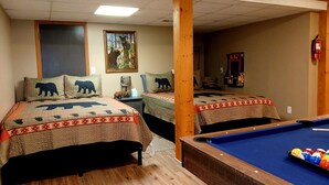 Een kamer met twee bedden, elk met een sprei met berenprint, een pooltafel en een lijst met een afbeelding van een beer aan de muur.