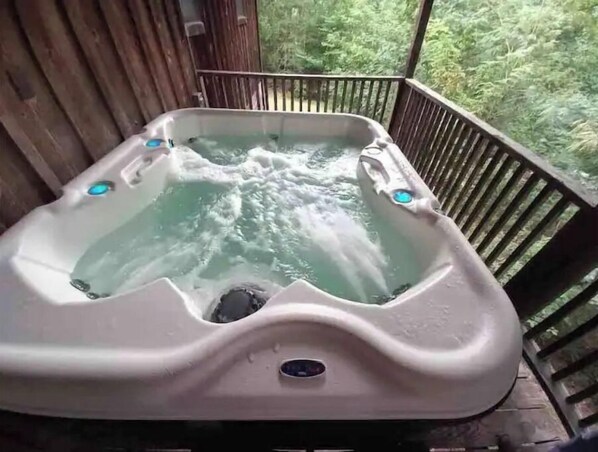 A hot tub with water jets on a wooden deck with a view of trees.