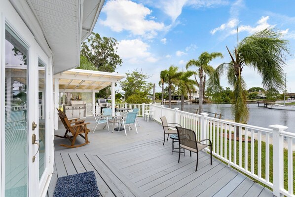 A covered outdoor deck with a grill, seating area, and a view of a lake.