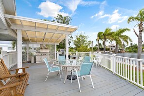 A covered outdoor deck with a grill, seating area, and a view of a body of water.