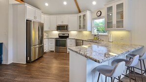 A modern kitchen with white cabinetry, stainless steel appliances, a granite countertop, and a bar area with stools. - Spacious 4BR/3BA with bunkhouse; perfect for family and friends! (Bryan)