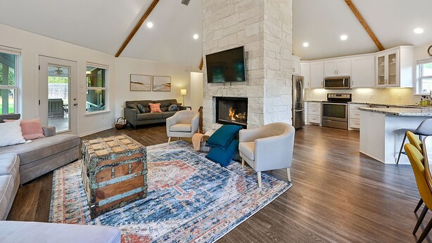 A spacious living room with a fireplace, a cozy seating area, and a modern kitchen with white cabinetry. - Spacious 4BR/3BA with bunkhouse; perfect for family and friends! (Bryan)