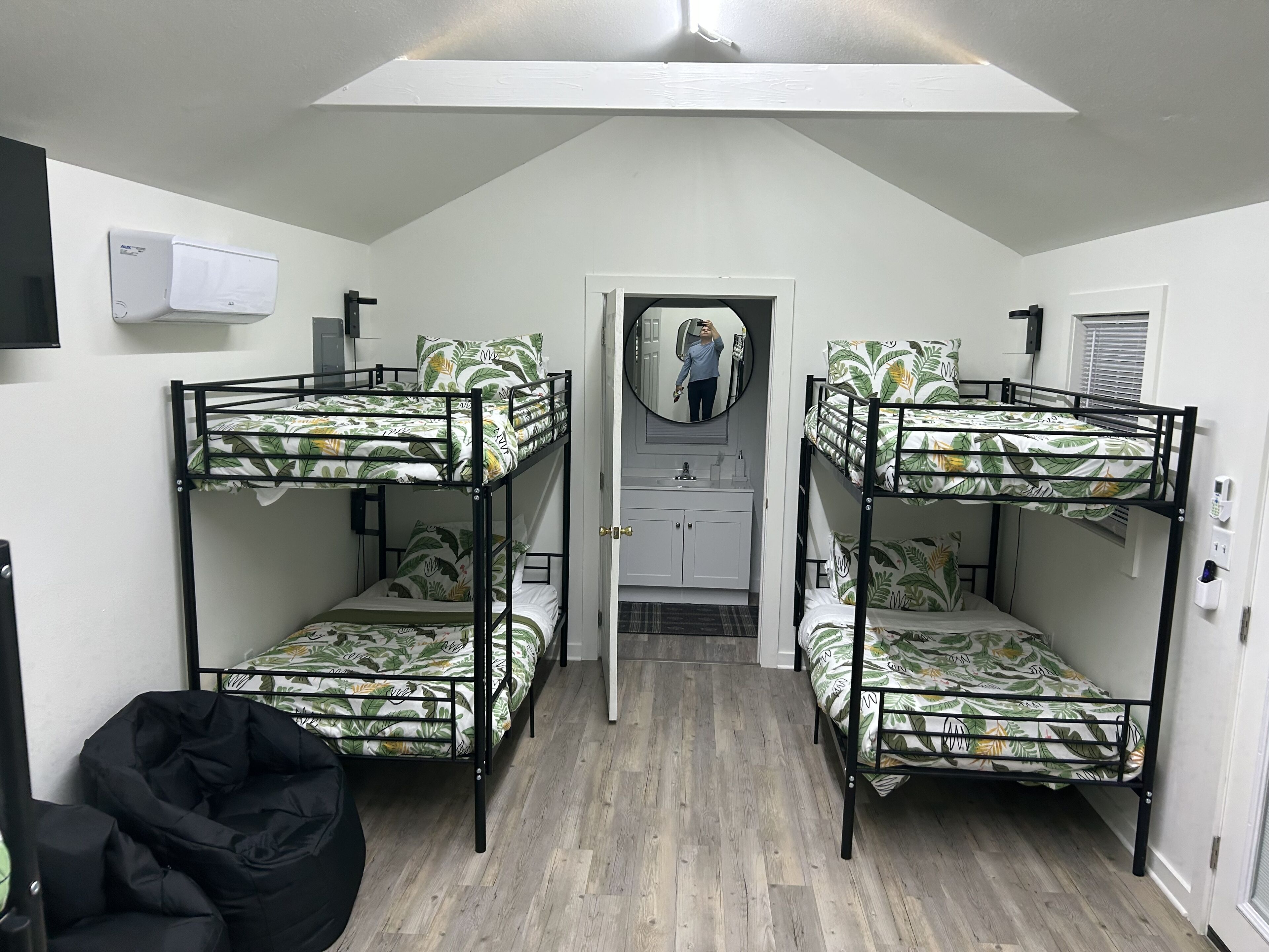 Ein Schlafsaalzimmer mit Etagenbetten, einer kleinen Küchenzeile, einem Spiegel und einem Deckenventilator.