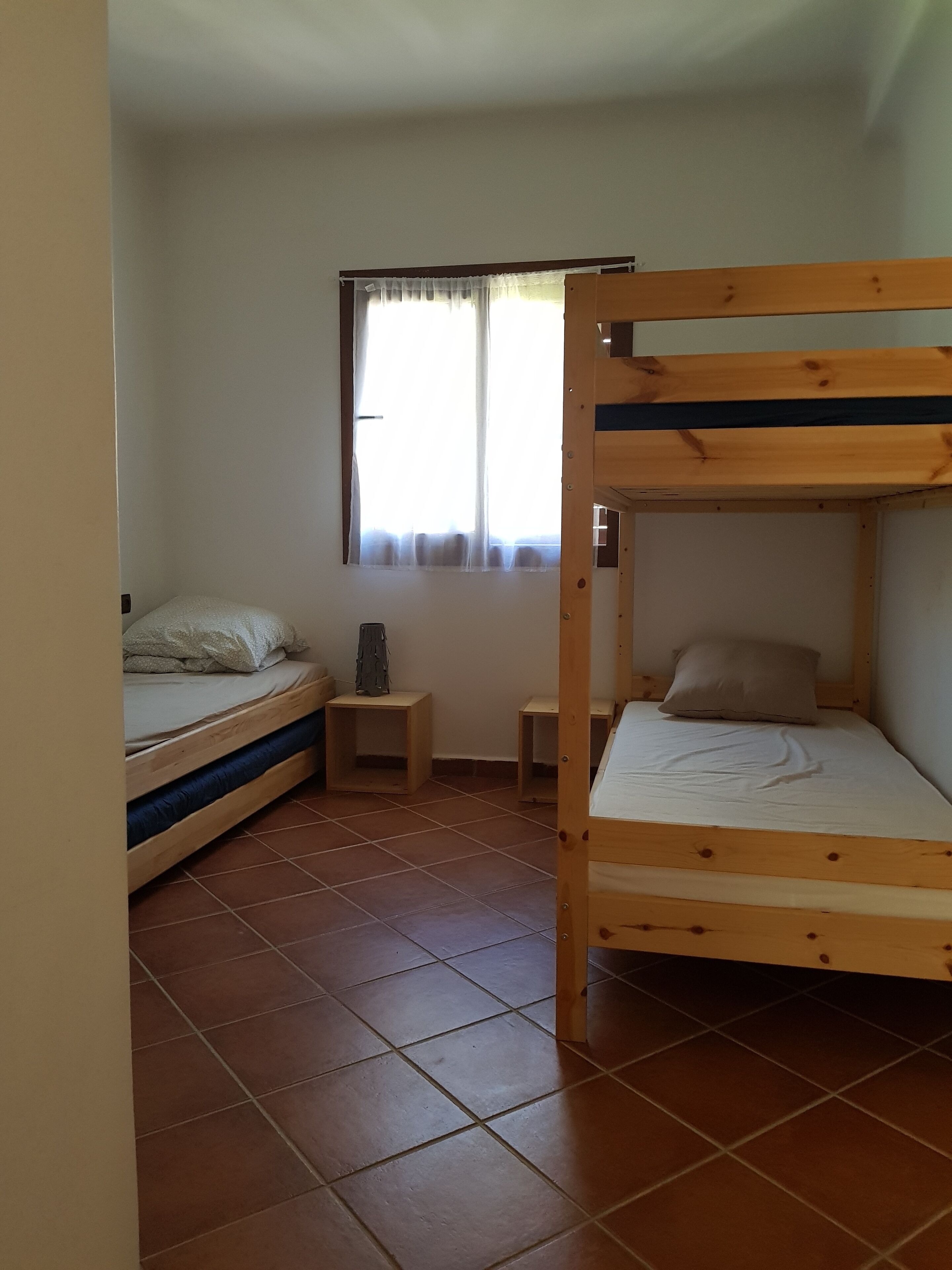 Un petit logement composé d’une seule pièce, comprenant un lit superposé, une petite table et une fenêtre avec des rideaux.