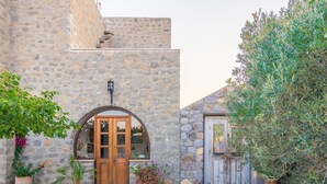 A stone building with a wooden door and arched entrance, surrounded by potted plants and olive trees. - Blue Vista Patmos Villa Margarita without the studios (Patmos)