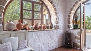 A rustic room with a stone wall, a wooden bench with cushions, and a window with multiple vases. - Blue Vista Patmos Villa Margarita without the studios (Patmos)